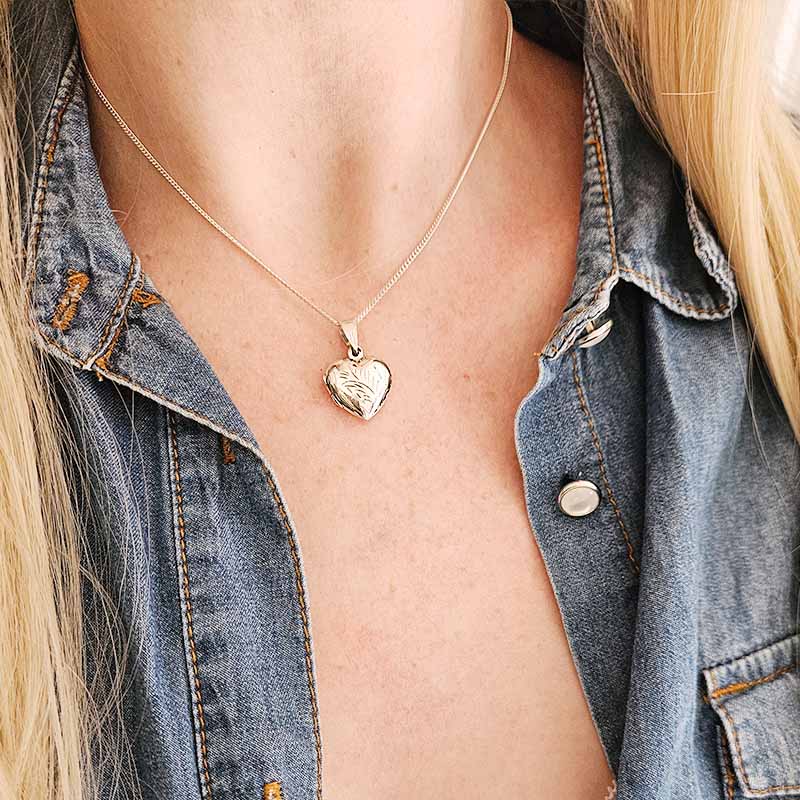 Person wearing a silver heart necklace with a heart pendant, visible under a denim jacket.