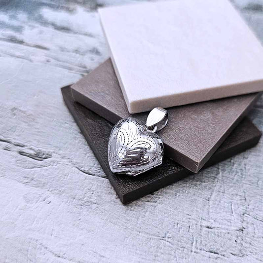Silver heart-shaped pendant on a textured surface with a book in the background