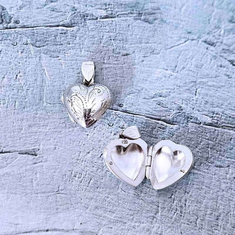 Two silver heart-shaped pendants on a textured light blue surface