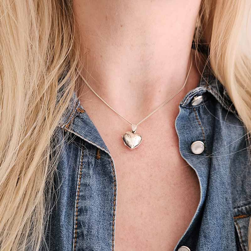 Person wearing a gold heart-shaped pendant necklace with a denim jacket.