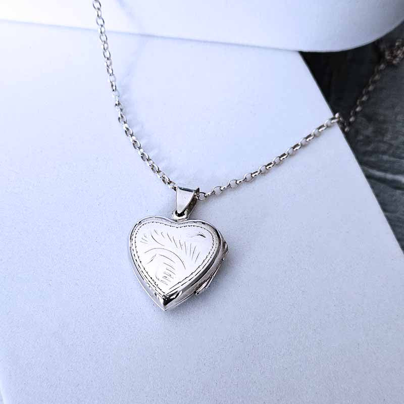 Heart-shaped silver locket on a chain against a light blue background