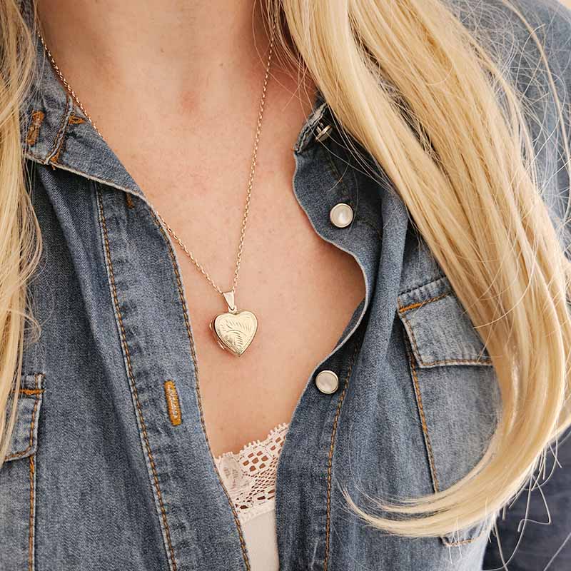 Person wearing a silver heart-shaped locket necklace with a denim jacket.