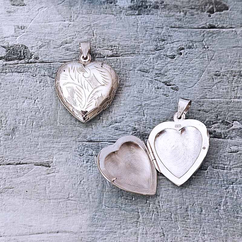 Three silver heart-shaped pendants on a textured gray surface