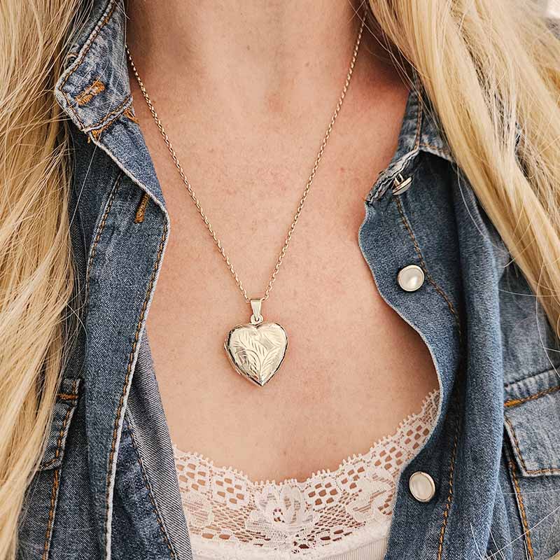Person wearing a silver heart-shaped locket necklace with a denim jacket and lace top.