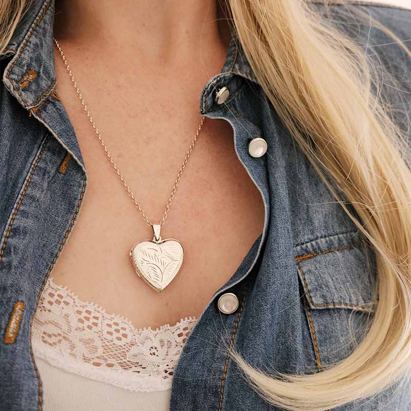 Heart-shaped locket necklace worn by a person with a denim jacket and lace top.