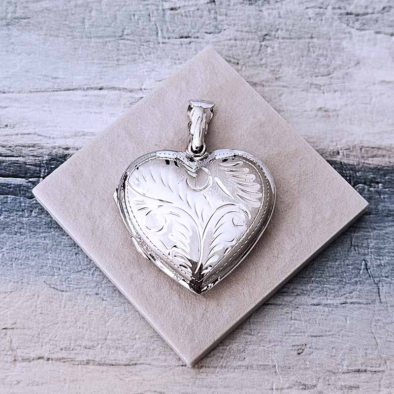 Silver heart-shaped pendant on a textured beige card with a rustic wooden background