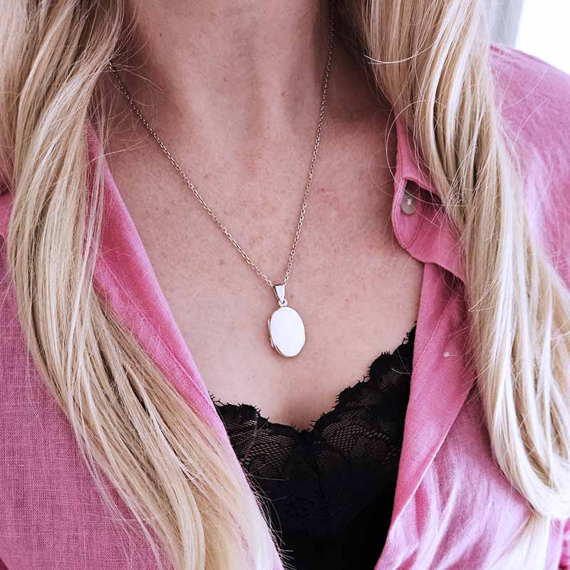 Person wearing a pink shirt with a silver locket necklace and black lace top underneath.