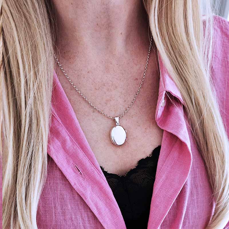 Person wearing a pink shirt with a necklace featuring an oval pendant.