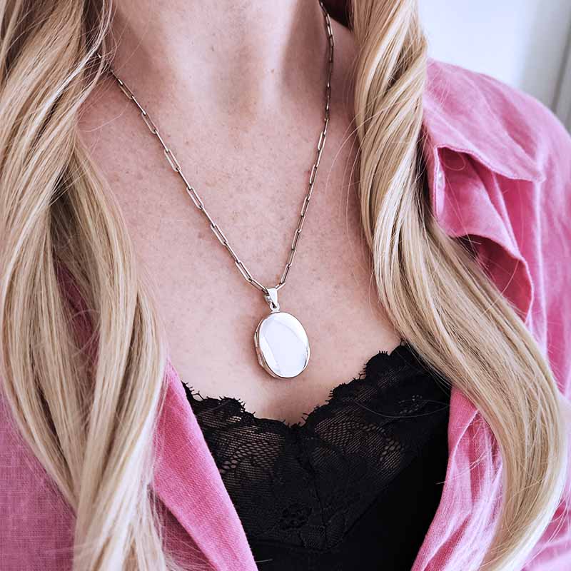 Person wearing a silver necklace with a pendant, pink shirt, and black lace top.