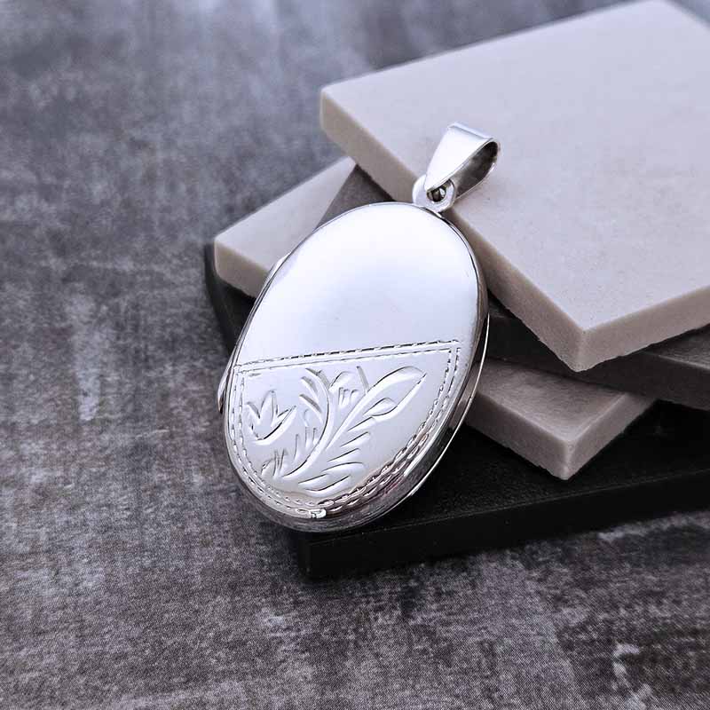 Silver locket with floral engraving on a textured surface