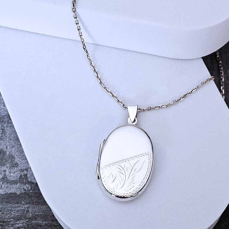 Silver locket necklace with engraved design on a white stand