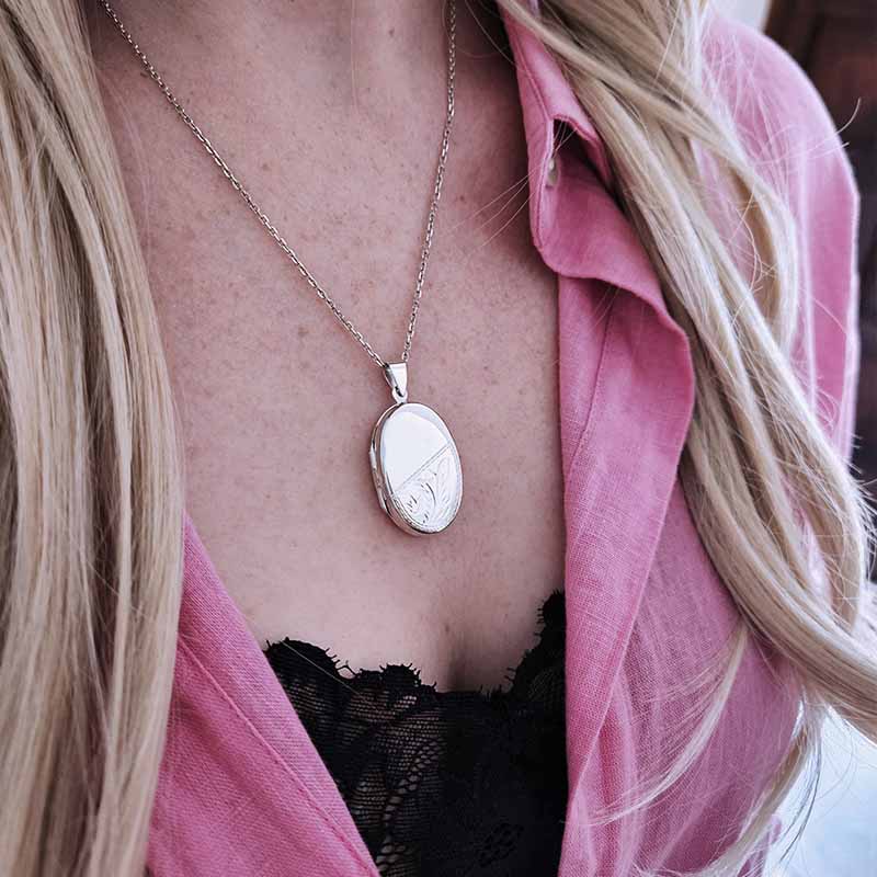 Person wearing a silver necklace with an oval pendant, pink shirt, and black lace top.