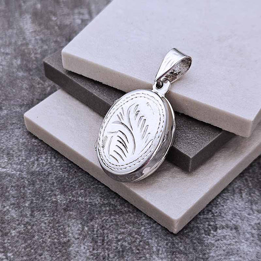 Silver locket with engraved design on a gray stone surface