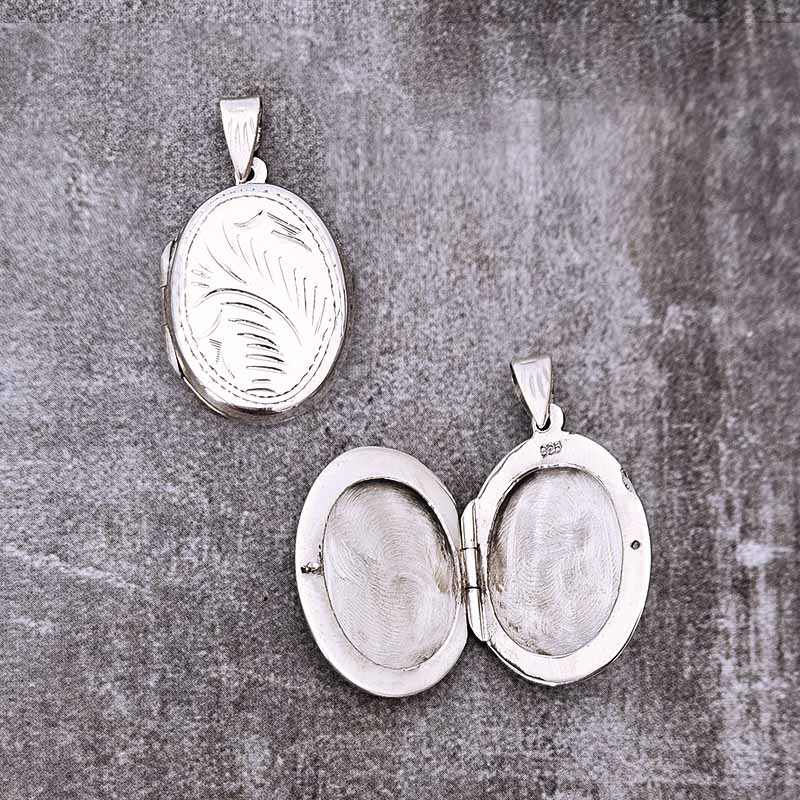 Two silver locket pendants on a textured gray surface