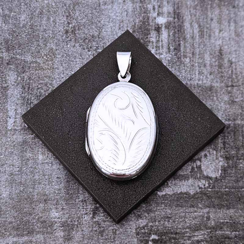 Silver locket with engraved design on a textured black surface