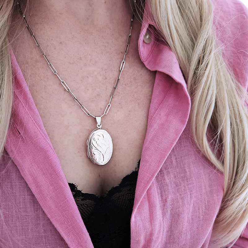 Person wearing a pink shirt with a silver locket necklace.