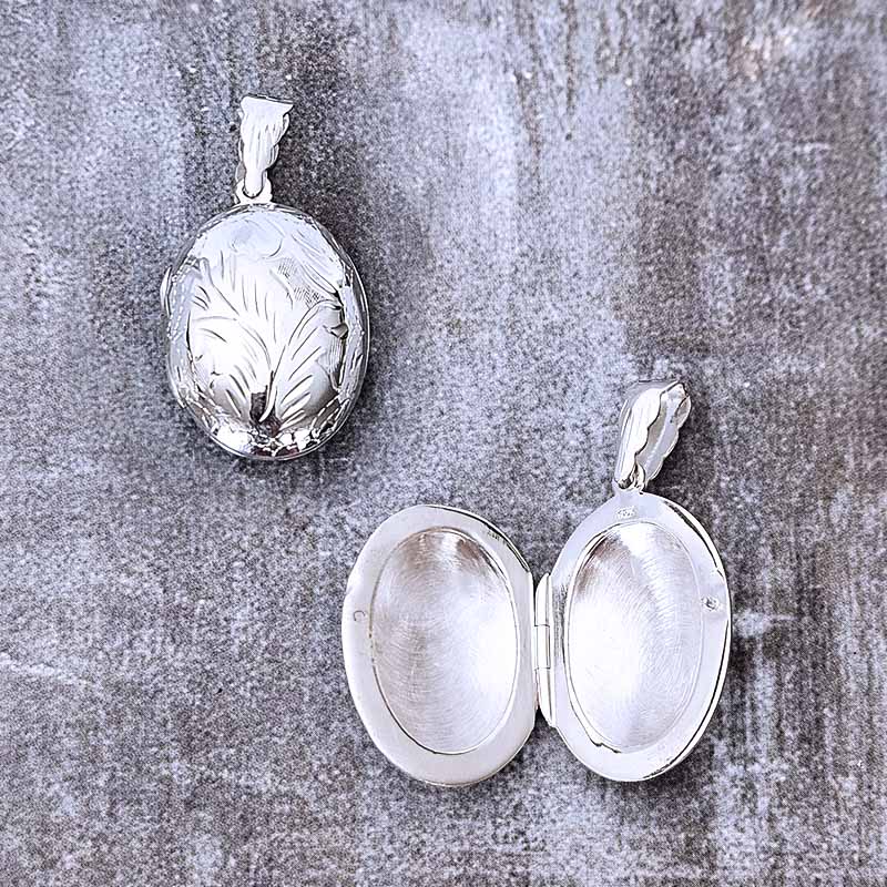 Silver locket with engraved design on a textured gray surface