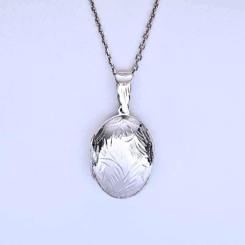 Silver locket with engraved design on a light purple background
