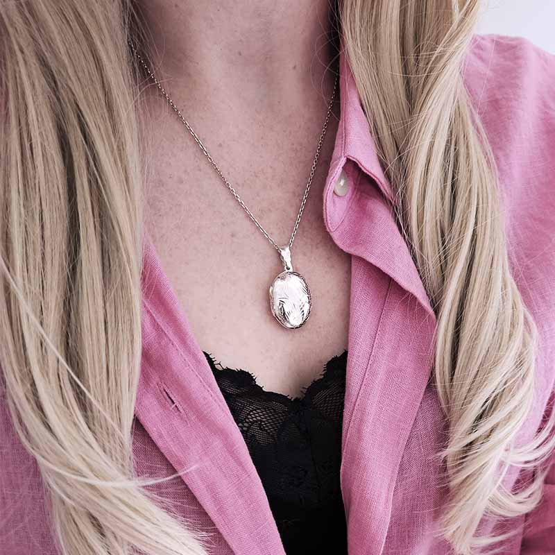 Person wearing a silver necklace with a pendant, pink shirt, and black lace top.