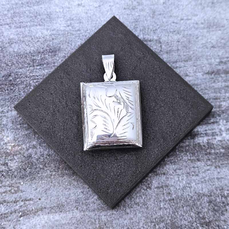 Silver pendant with leaf design on a gray textured surface