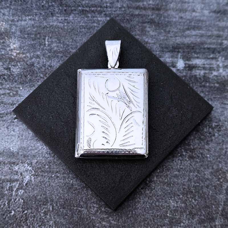 Silver pendant with engraved design on a black square background
