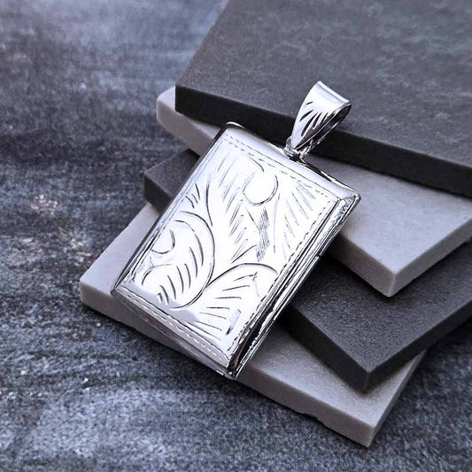 Silver pendant with leaf design on a gray stone surface