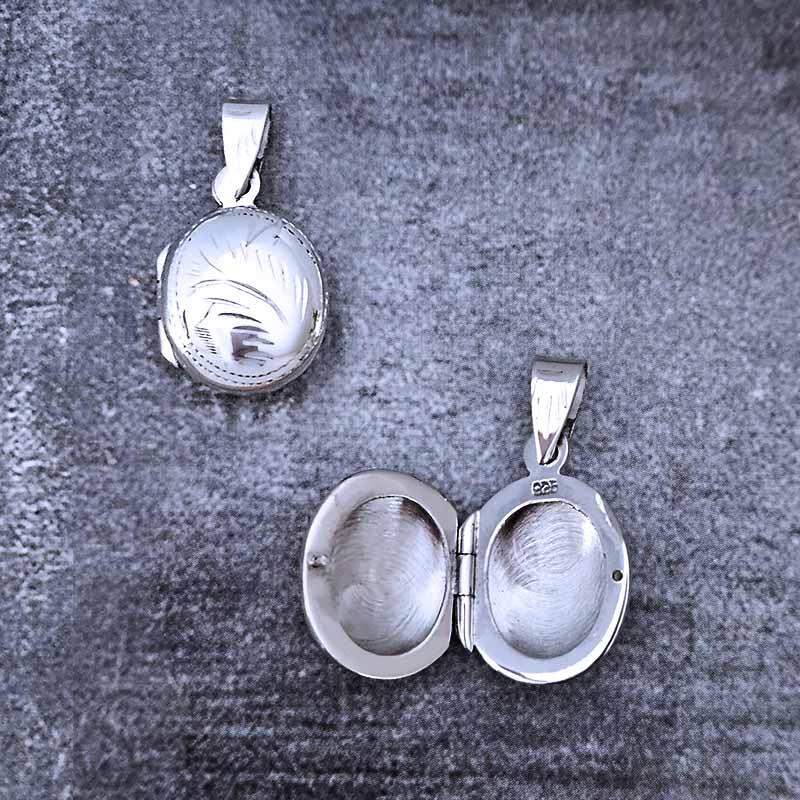 Silver locket with engraved design on a textured gray surface