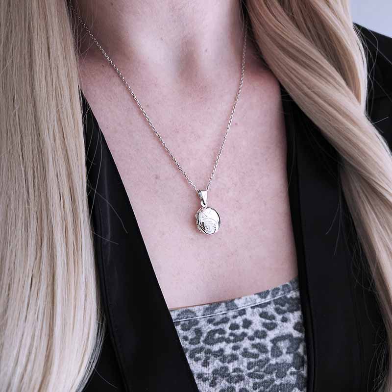Person wearing a silver necklace with a pendant, visible skin and black top.