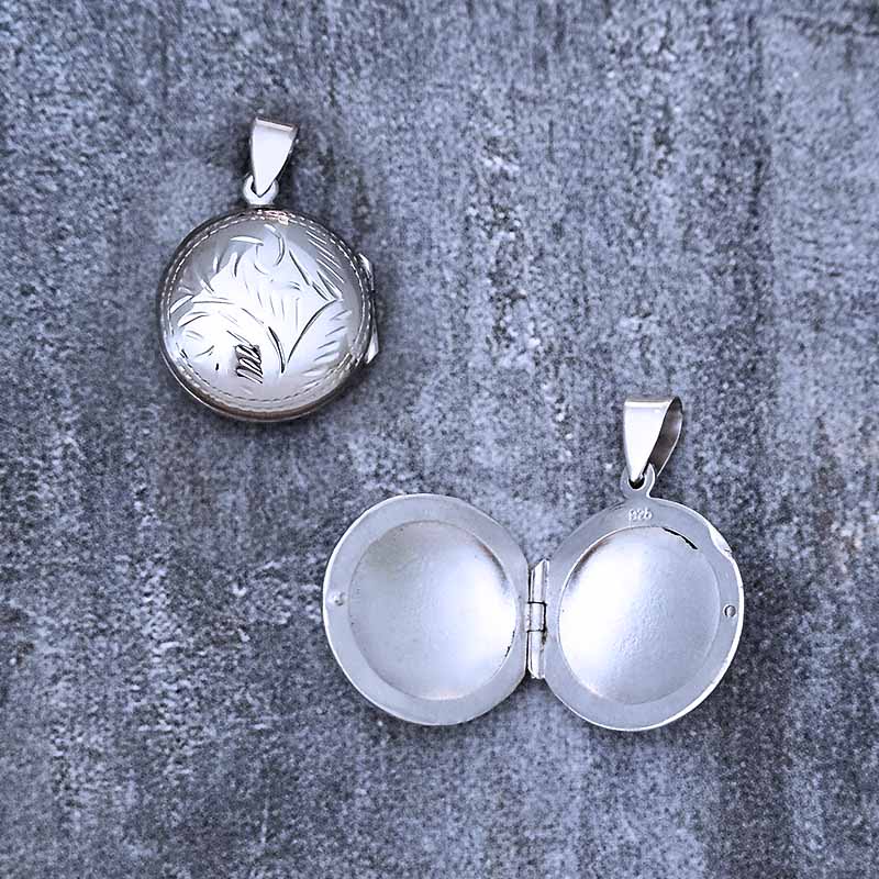 Silver locket with engraved design on a textured gray surface