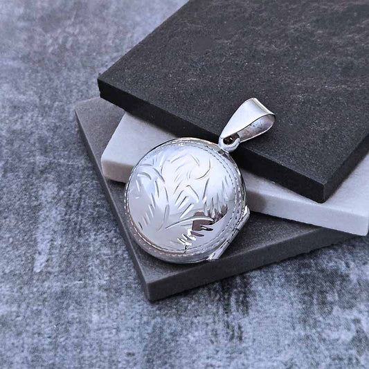 Silver pendant with engraved design on a gray surface