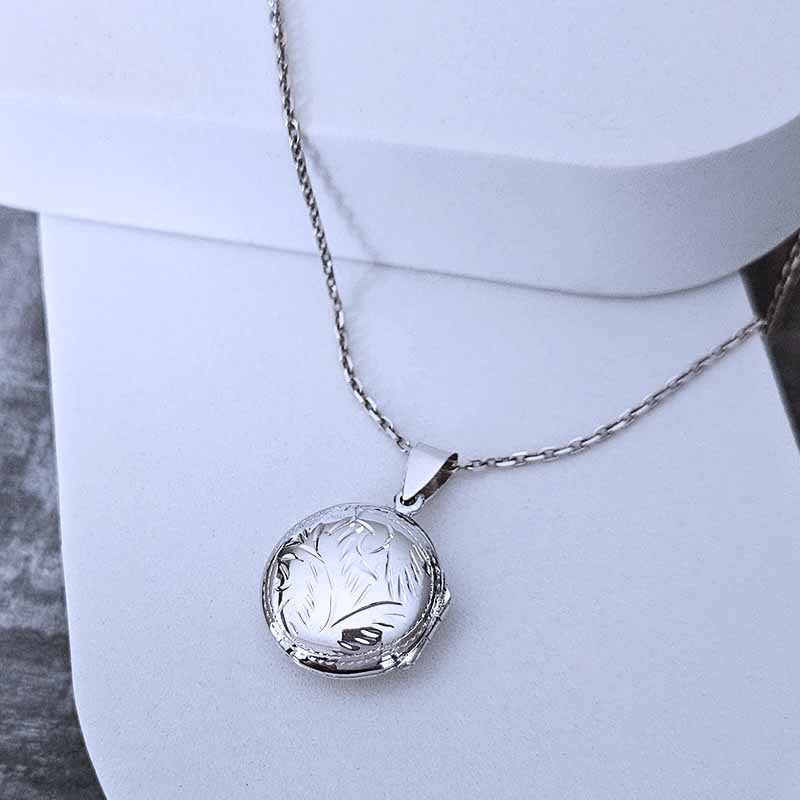 Silver necklace with a round engraved pendant on a white mannequin.