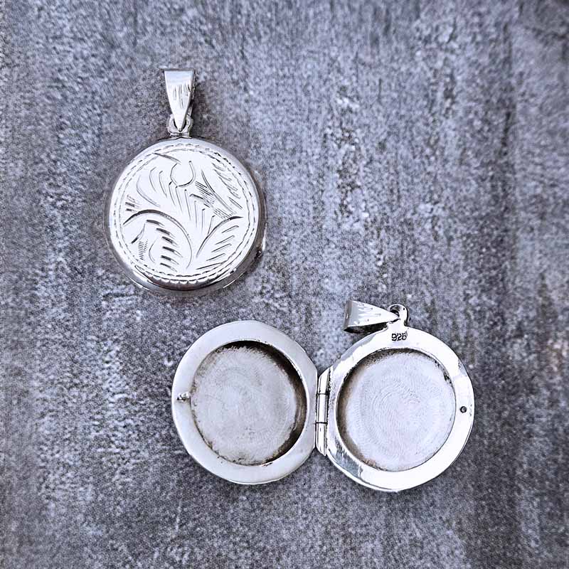 Silver locket with engraved design on a textured gray surface