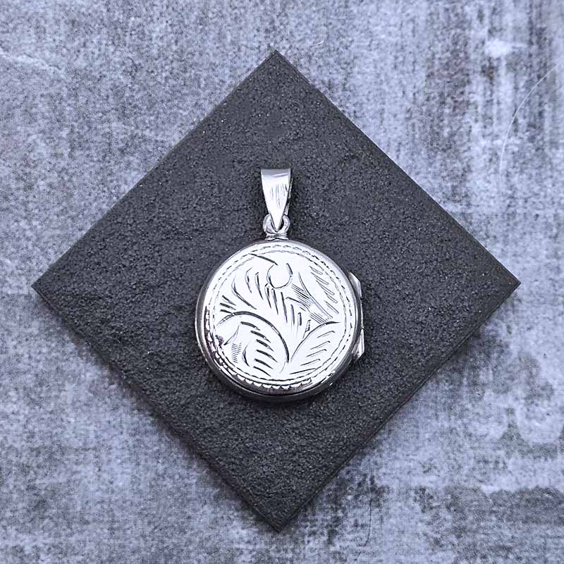 Silver pendant with intricate design on a dark gray square background