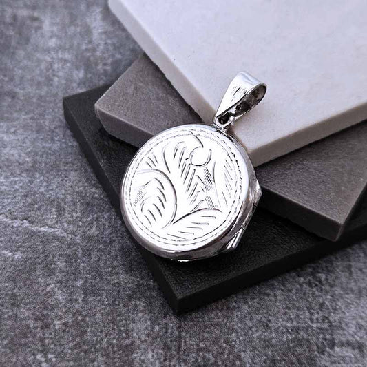 Silver pendant with engraved design on a gray surface