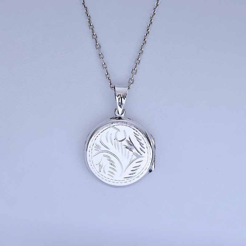 Silver locket with engraved design on a light gray background
