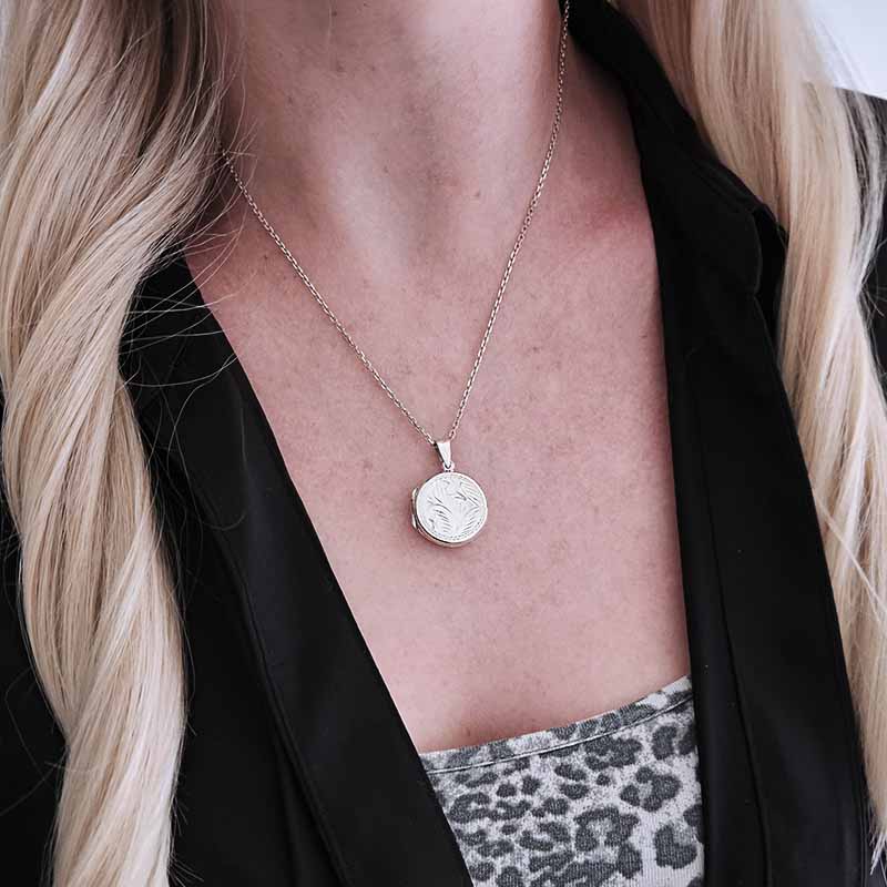 Person wearing a silver necklace with a round pendant, black jacket, and leopard print top.