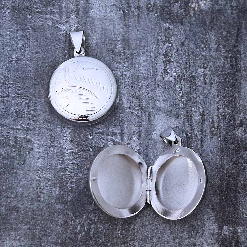 Silver locket with engraved design on a textured gray surface