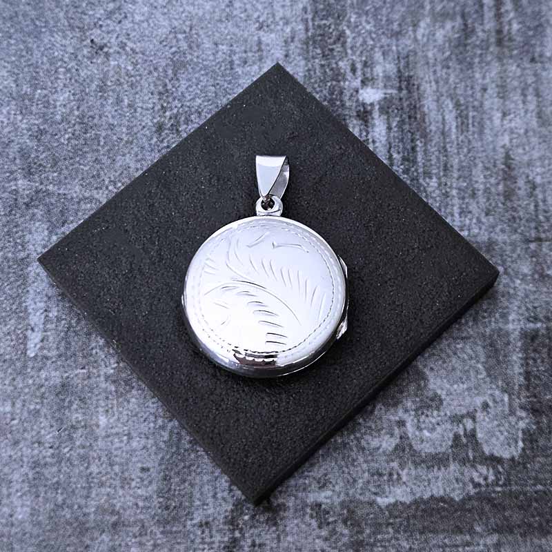 Silver locket with engraved design on a black square base against a textured gray background
