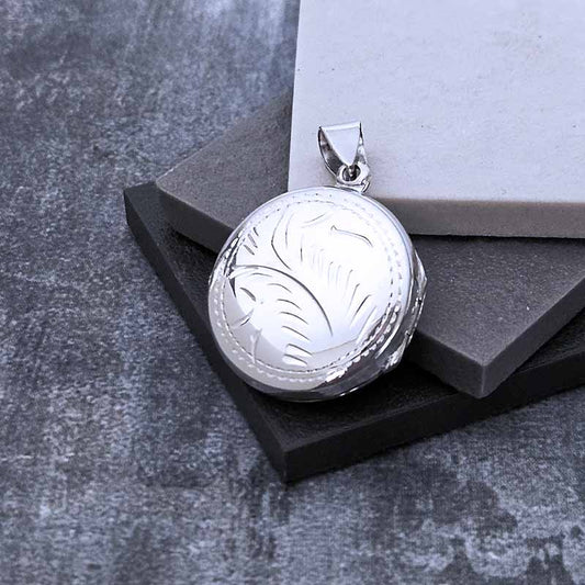 Silver pendant with engraved design on a gray surface