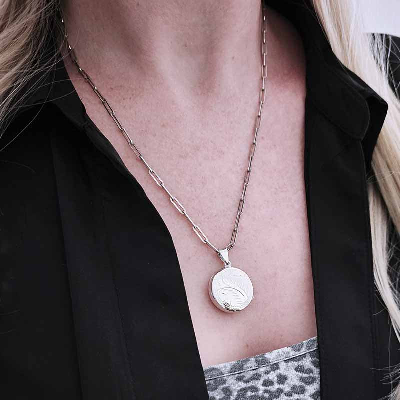 Silver necklace with a round pendant worn by a person against a black background