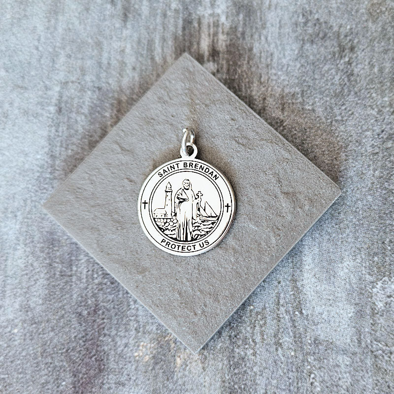 Silver pendant with religious design on a gray stone surface