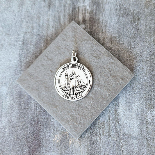 Silver pendant with religious design on a gray stone surface