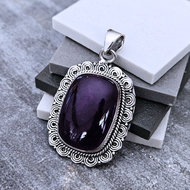 Purple stone pendant with silver frame on a textured surface