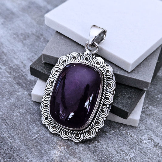 Purple stone pendant with silver frame on a textured surface