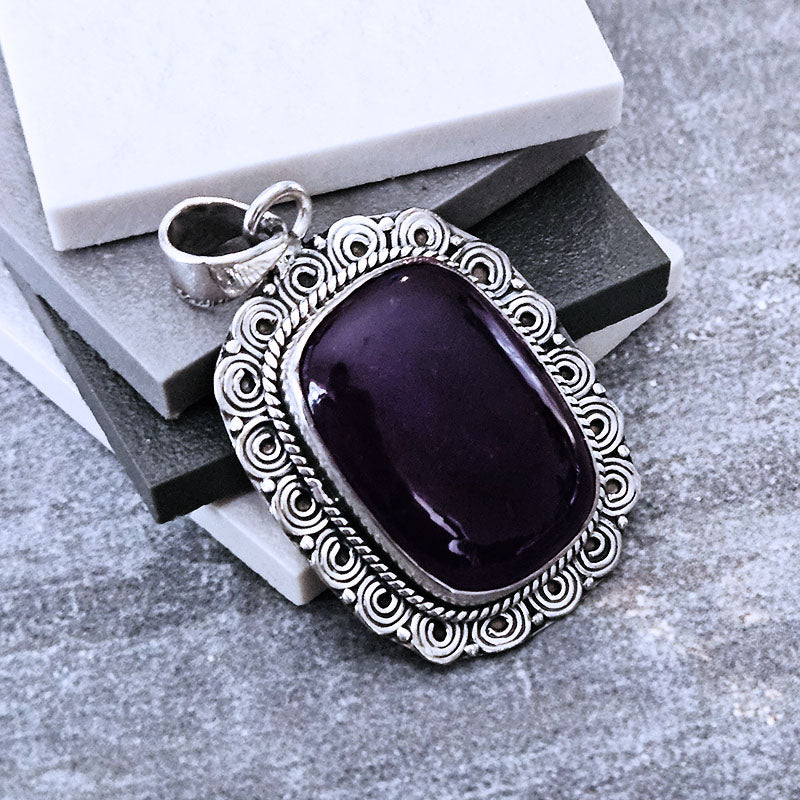 Amethyst stone pendant with silver frame on a textured surface