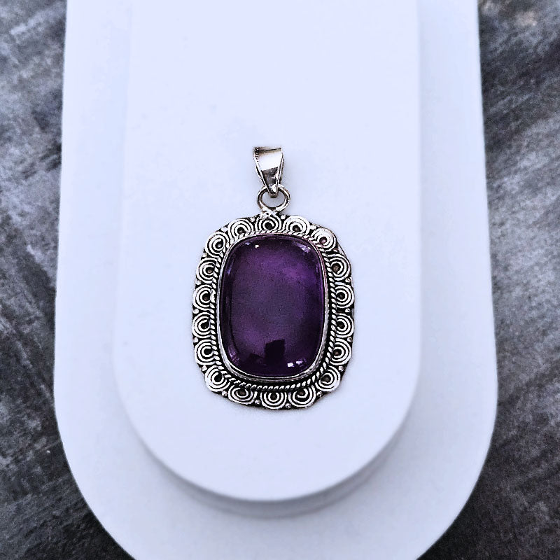 Amethyst stone pendant with silver frame on a textured surface