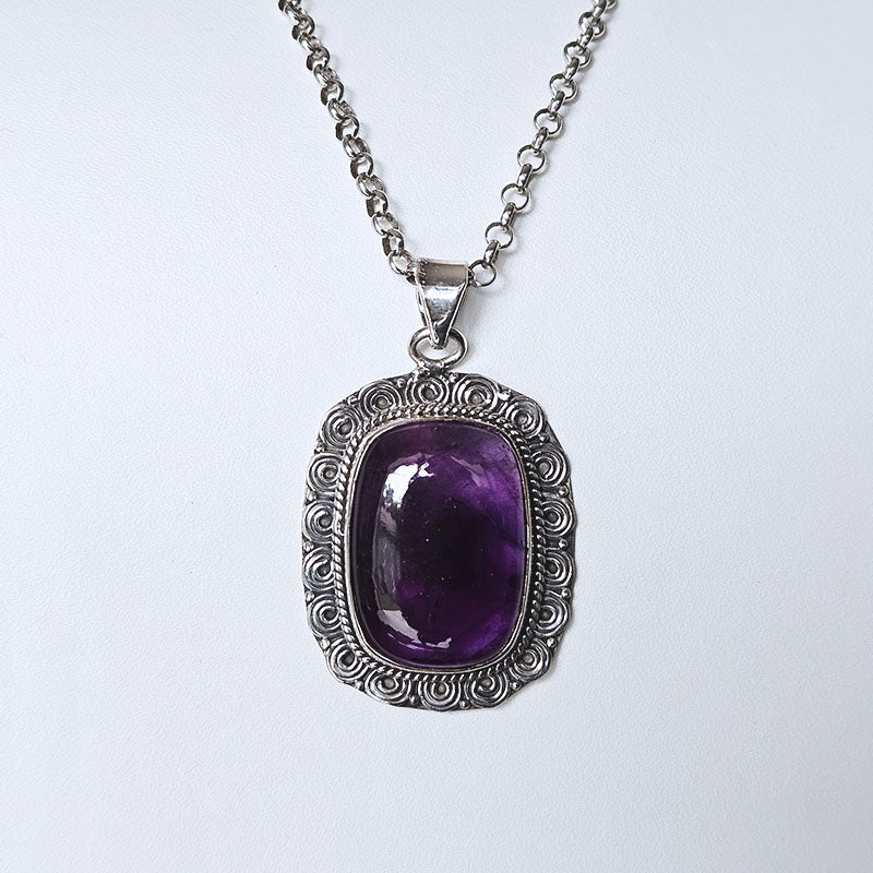 Purple gemstone pendant on a silver chain against a white background