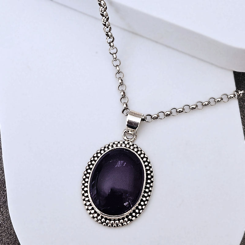A silver-tone chain necklace with an oval bezel pendant featuring a dark purple stone, displayed on a white jewelry stand.