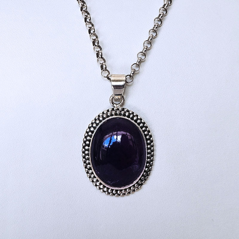 A silver-tone chain necklace with an oval bezel pendant featuring a deep dark purple cabochon stone, set against a plain light background.