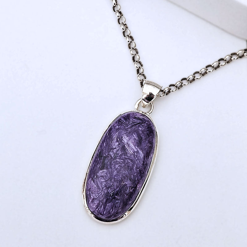 A silver chain necklace with an oval pendant featuring a textured purple stone, displayed on a clean white background.
